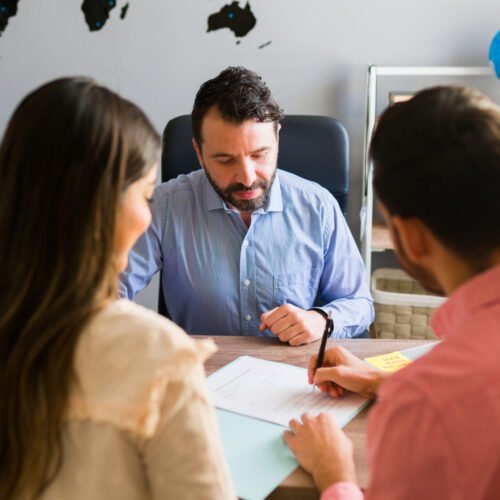 You got a deal. Young man signing a sales contract for a holiday vacation with his wife. Sales representative closing a deal for a timeshare sale with some customers at the travel agency