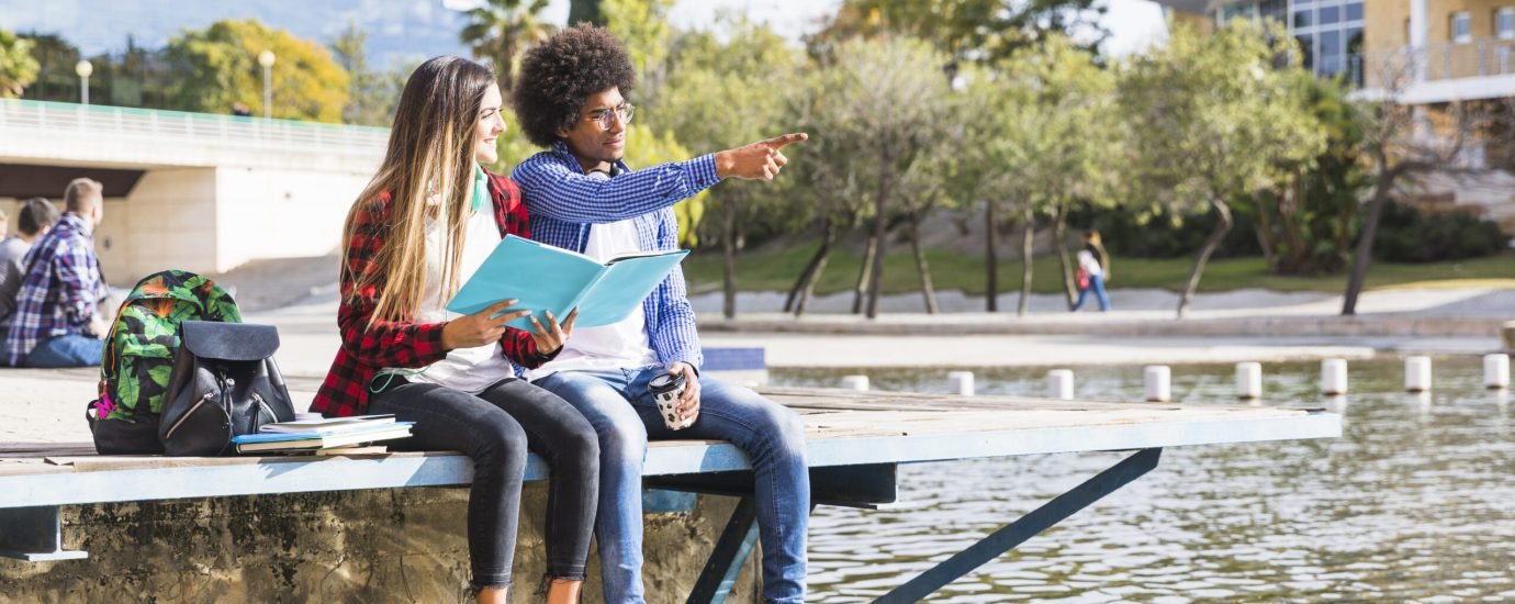 teenage-girl-holding-book-hand-looking-his-boyfriend-showing-something-near-lake teenage-girl-holding-book-hand-looking-his-boyfriend-showing-something-near-lake